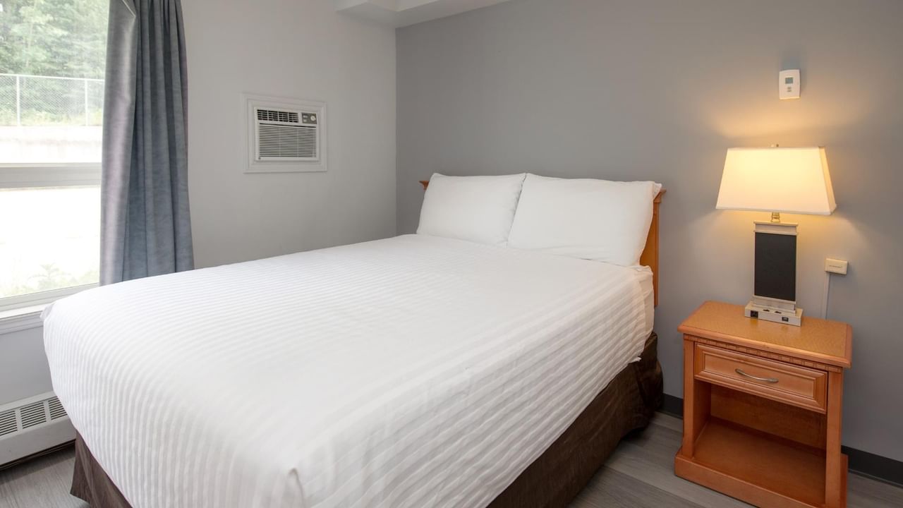 A bedroom with a bed, a nightstand with a lamp, and a window with curtains.