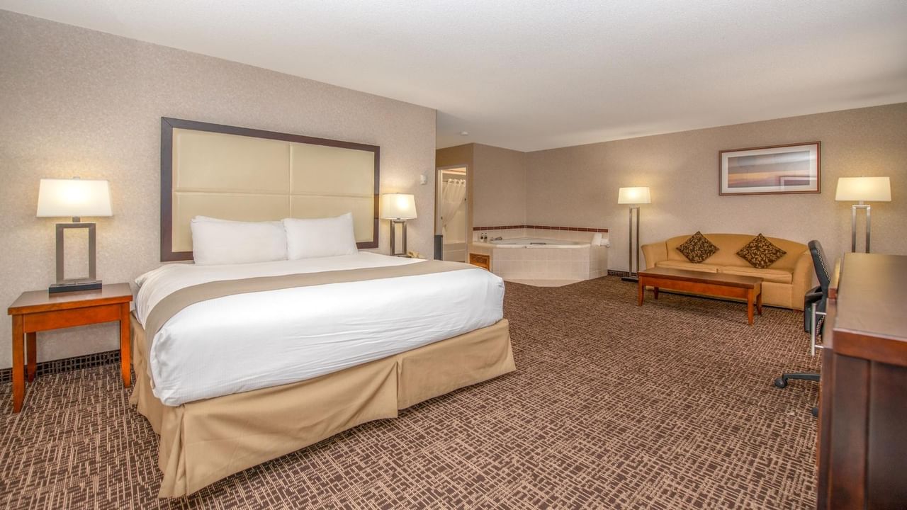 A hotel room with a large bed, couch, coffee table, and a jetted tub.
