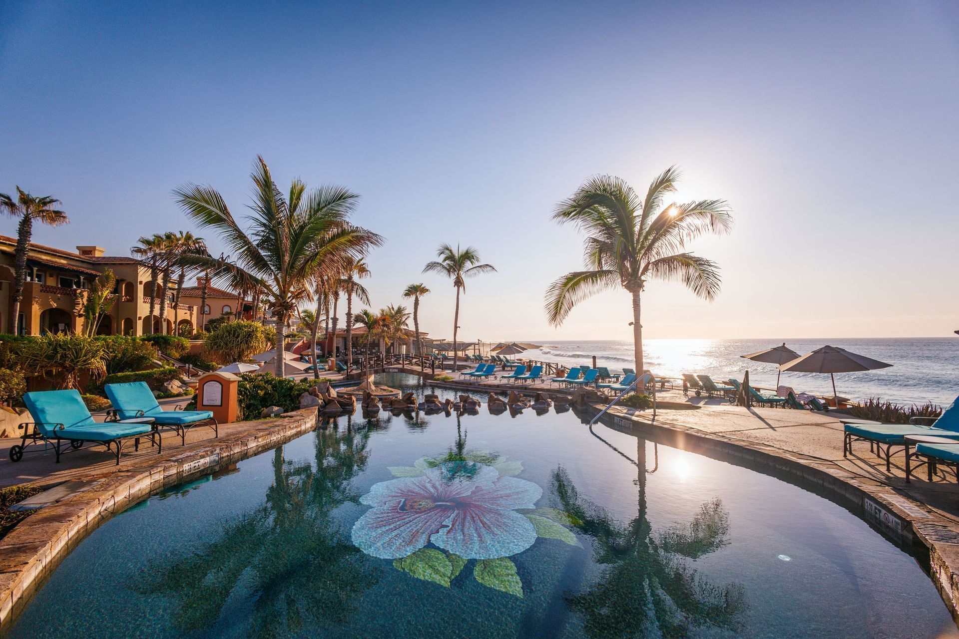 Outdoor pool with flower mosaic, palm trees, and lounge chairs glowing at sunset in Hacienda del Mar Los Cabos