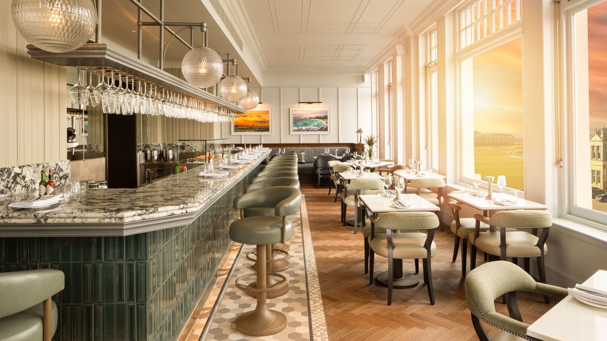 Counter with stools & dining tables by tall windows framing a stunning sunset view at Ondine Oyster & Grill in Seaton House