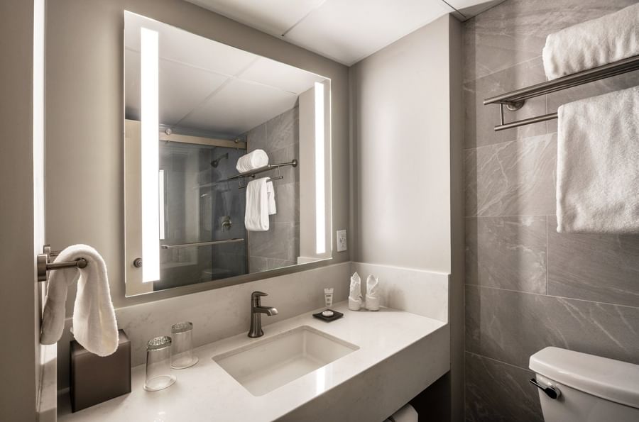 Lighted mirror by a white sink and towels near a stone-walled bathroom in Premier Room at Warwick Seattle