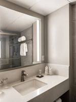 Lighted mirror by a white sink and towels near a stone-walled bathroom in Premier Room at Warwick Seattle