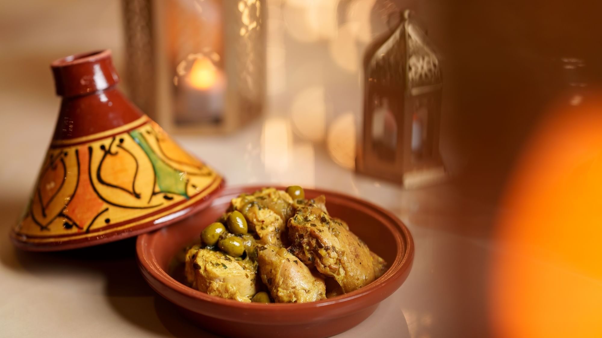 Close-up of Moroccan chicken tagine with olives in a clay pot with decorative lanterns at Paramount Hotel Dubai