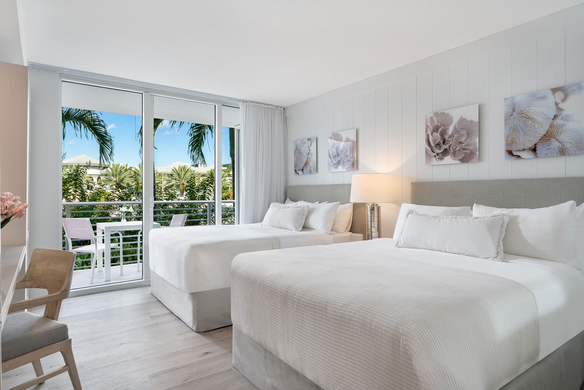 A bright and airy hotel room with two twin beds, a balcony with palm tree views, and modern decor.