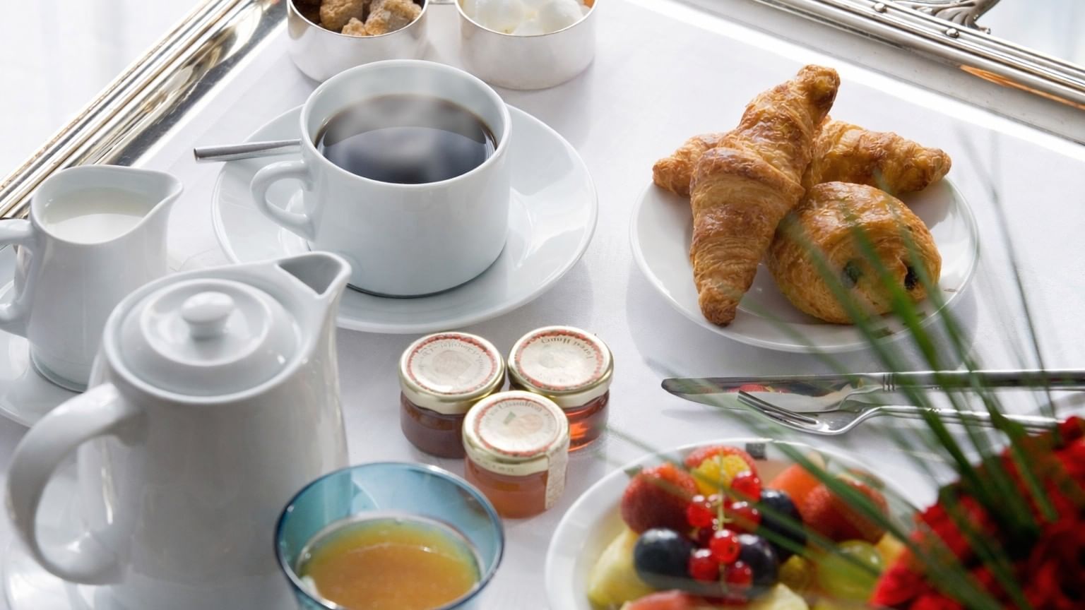 Hot coffee by croissants and fresh fruit on a white tray in Breakfast & 24-Hour Room Service at Warwick Paris Champs Elysées