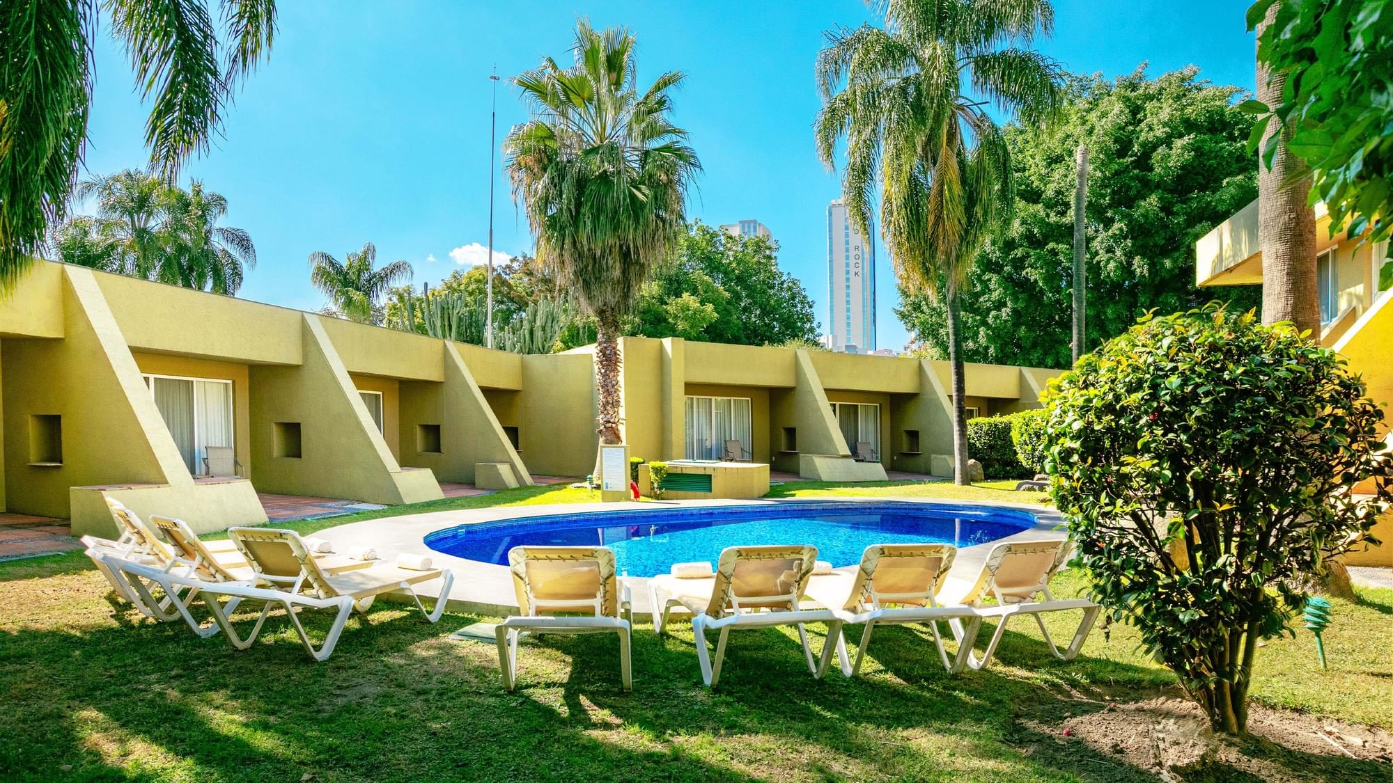 Tumbonas alrededor de la piscina con edificio amarillo del hotel en Camino Real Guadalajara