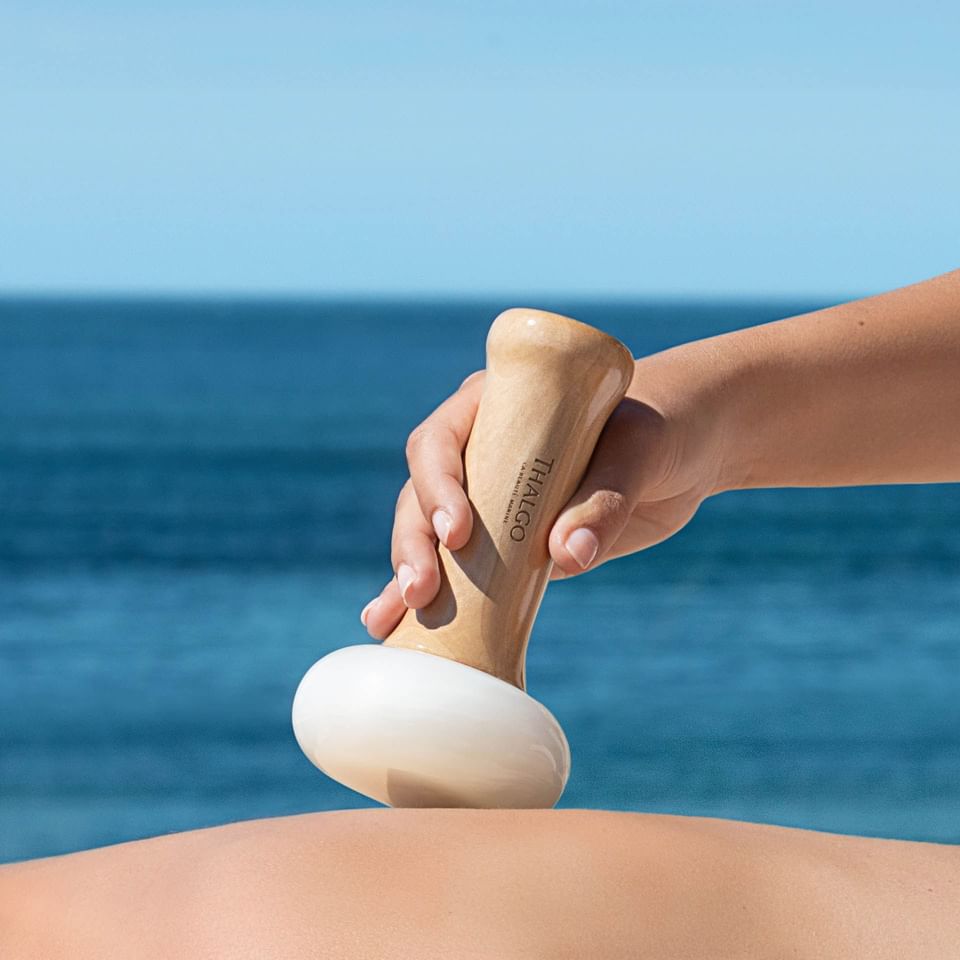 A hand uses a massage tool on a person's back with an ocean backdrop at The Saujana Hotel Kuala Lumpur