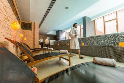 Hombre con bata junto a camastros de madera bajo lámparas cálidas en Noi Spa de NOI Vitacura