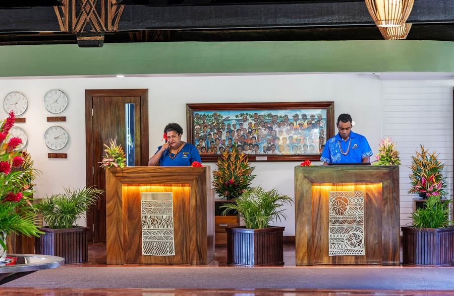 Two receptionists standing behind wooden counters at The Naviti Resort Fiji.