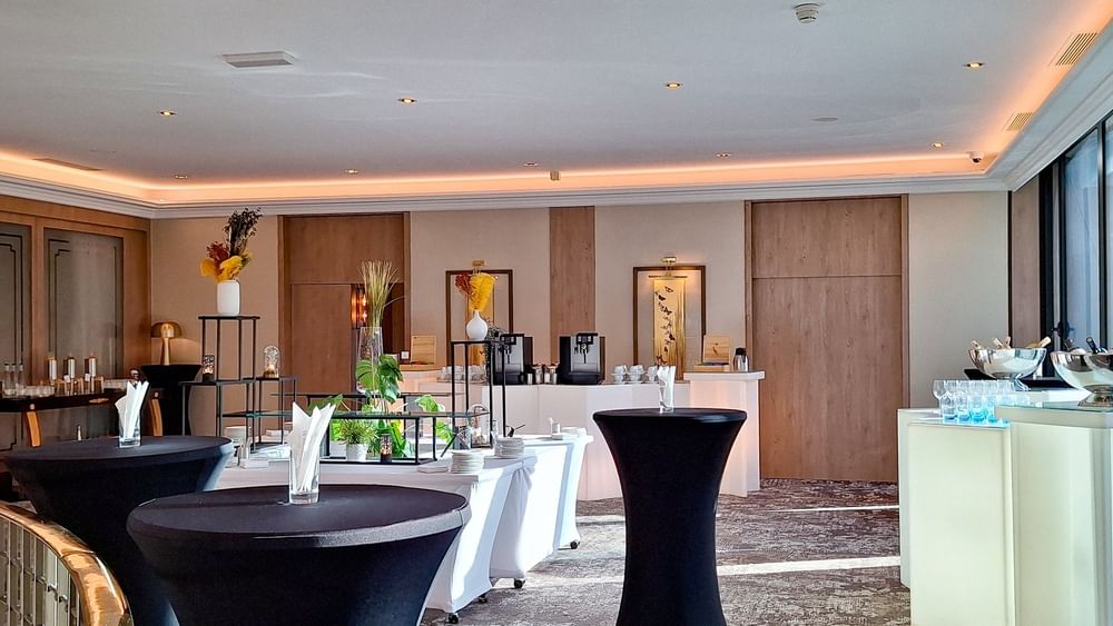 Black bistro tables by white buffet stations under warm recessed lighting in Foyer Mezzanine at Warwick Geneva