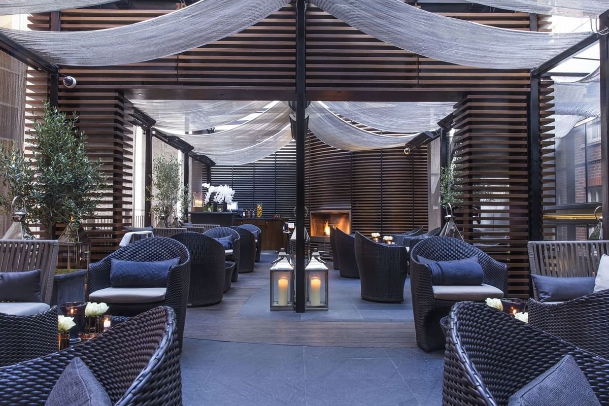 Elegant May Fair Kitchen terrace with wicker seating, cushions, soft drapes, and candlelight at The May Fair Hotel