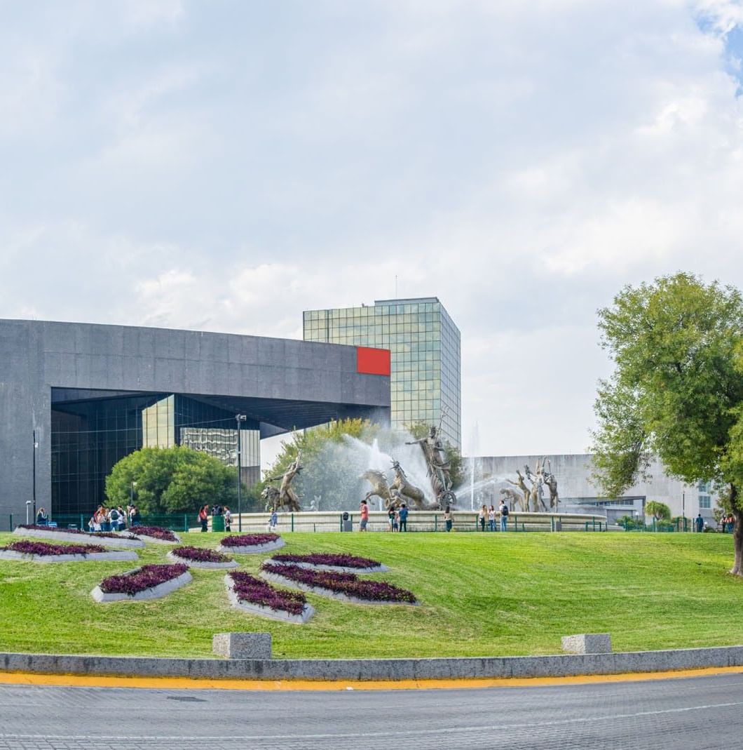 Macroplaza fountain with bronze statues in front of a sleek glass building at Camino Real Fashion Drive, Monterrey