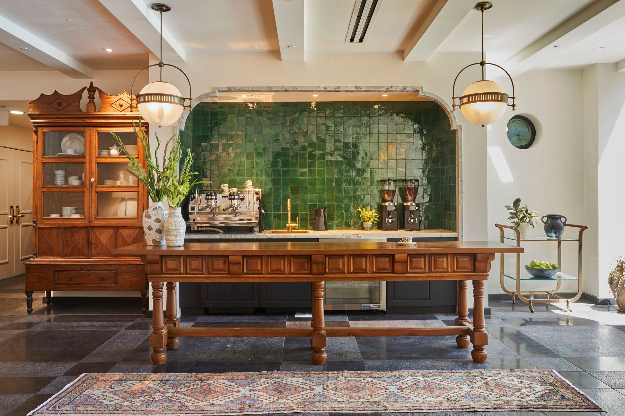 Refreshment area with a large wooden table, green tiled wall, and vintage-style lighting at El Prado Hotel