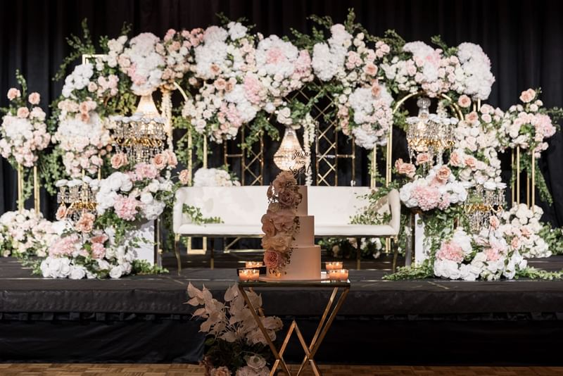 Wedding cake on a stand with a floral arch and chandeliers at Sofitel Brisbane Central