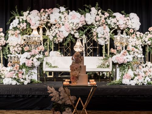 wedding stage with floral arches, chandeliers, and a tiered cake at Sofitel Brisbane Central