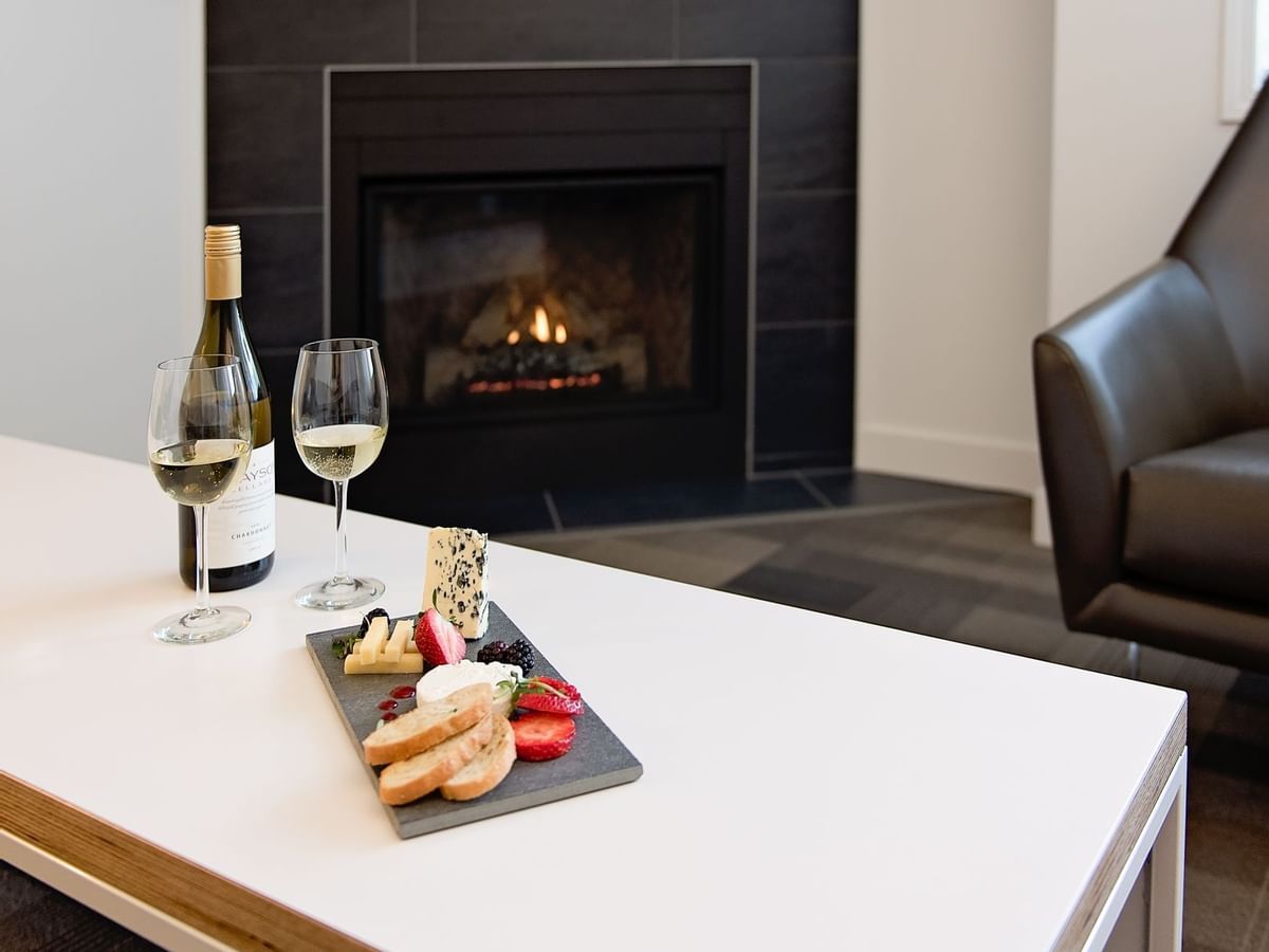 Table with meat and cheese plate and white wine next to fireplace