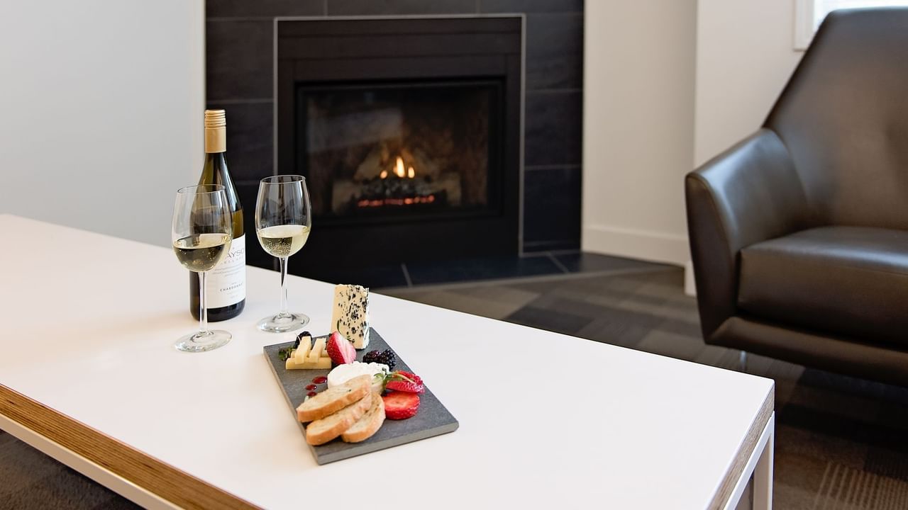 Table with meat and cheese plate and white wine next to fireplace