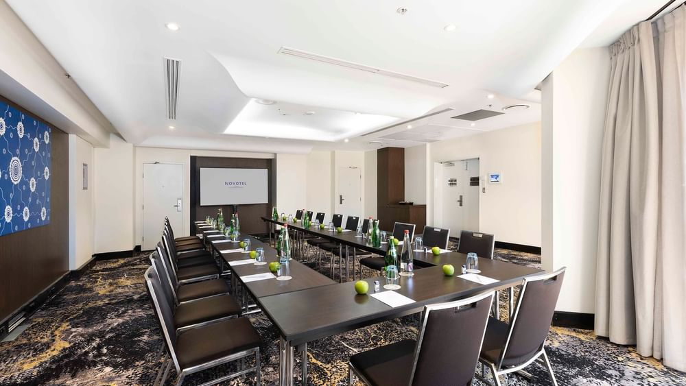 U-shaped table set-up with a projector screen and carpeted floors in The Yarra Room at Novotel Sydney on Darling Harbour