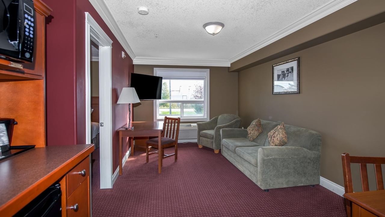 Spacious suite with gray sofa, wooden furniture, burgundy carpet, and natural light at Coast Edson Hotel.