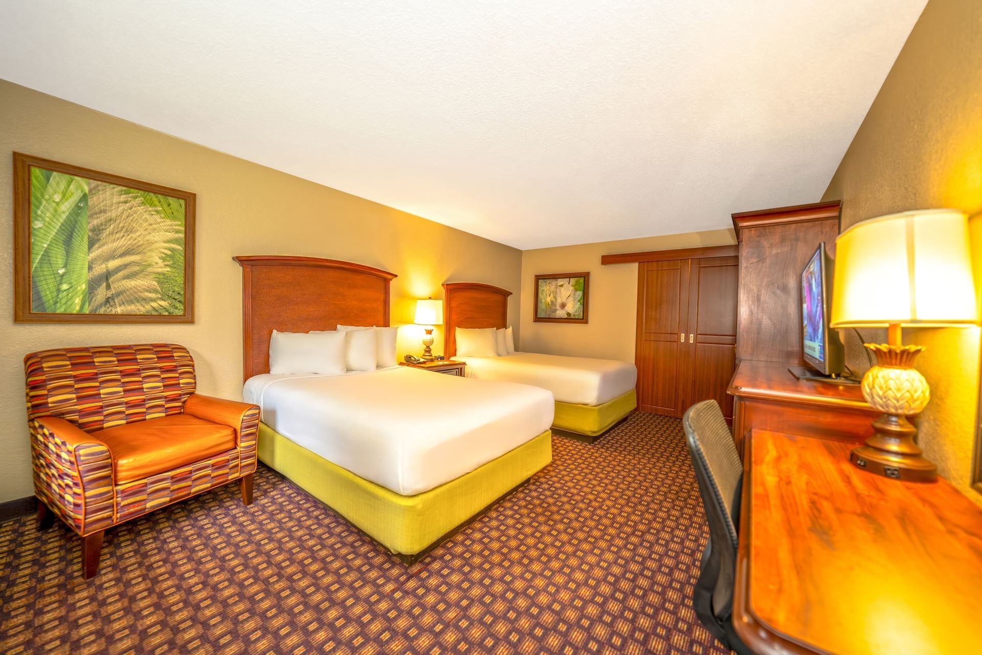 A hotel room with two double beds, a desk, chair, and lamp.