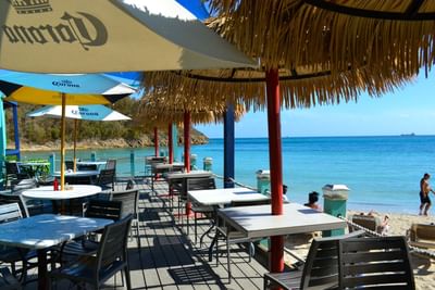Outdoor dining tables under Corona umbrellas and thatch roofs next to the ocean in Caribbean Fusion at Emerald Beach Resort