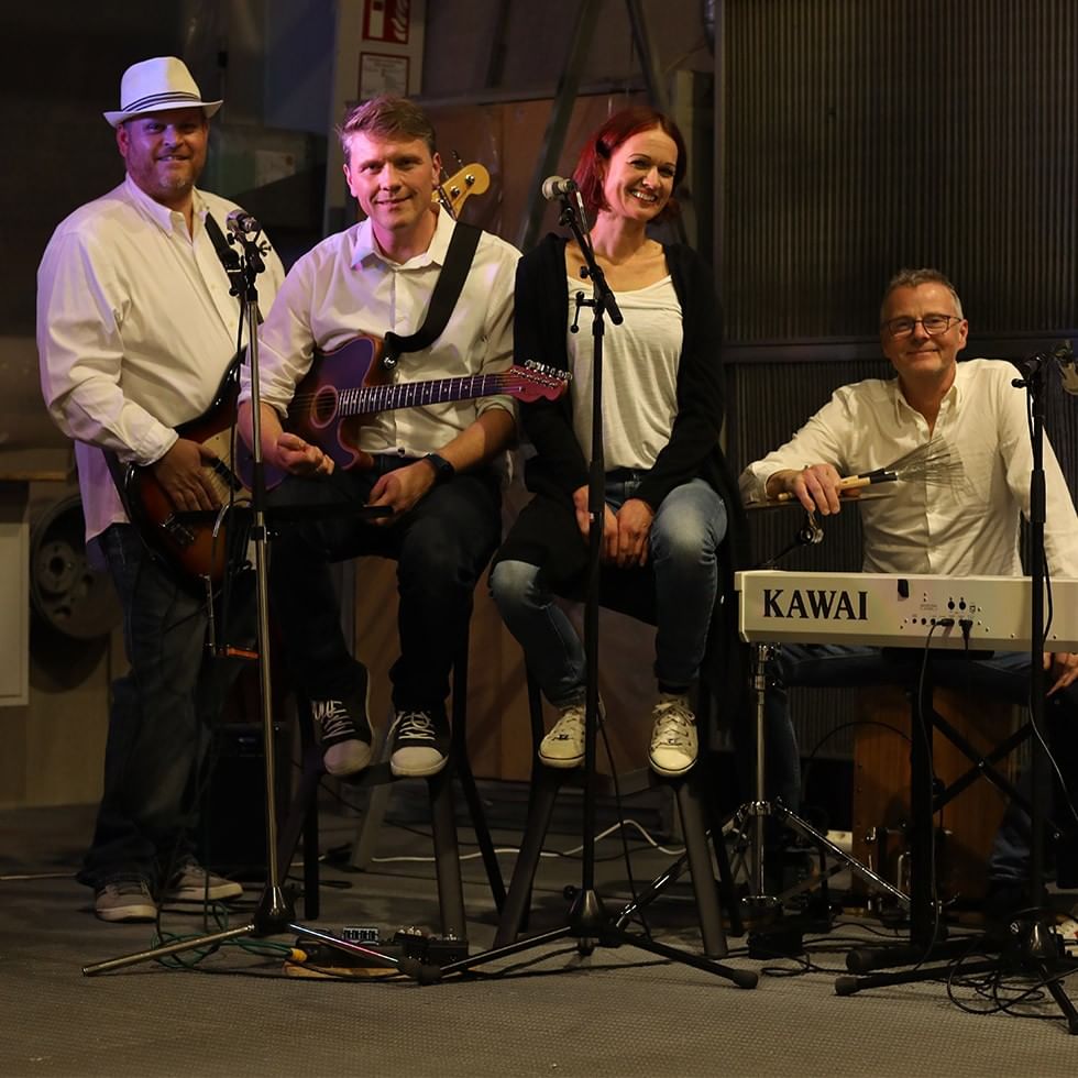Four musicians with guitars, a keyboard, and a percussion instrument performing on stage.