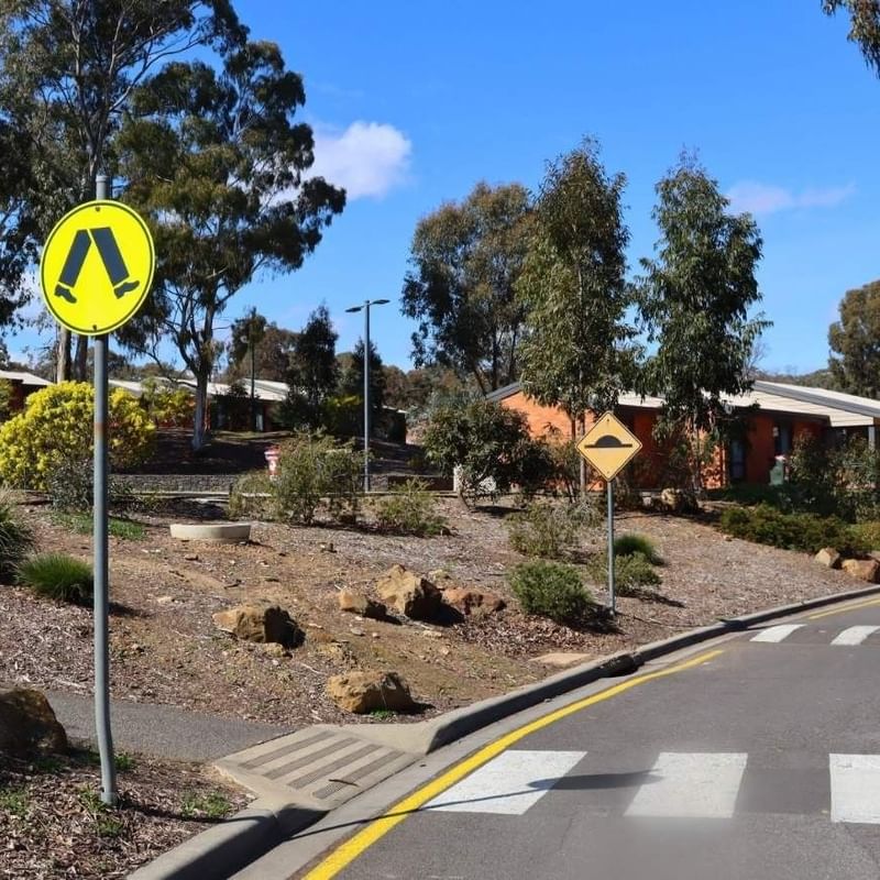La Trobe University Terraces entrance with trees and pedestrian crossing signs.