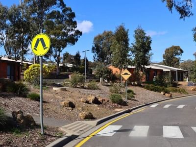 La Trobe University Terraces entrance with trees and pedestrian crossing signs.