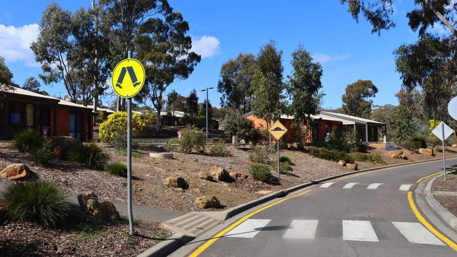 La Trobe University Terraces entrance with trees and pedestrian crossing signs.