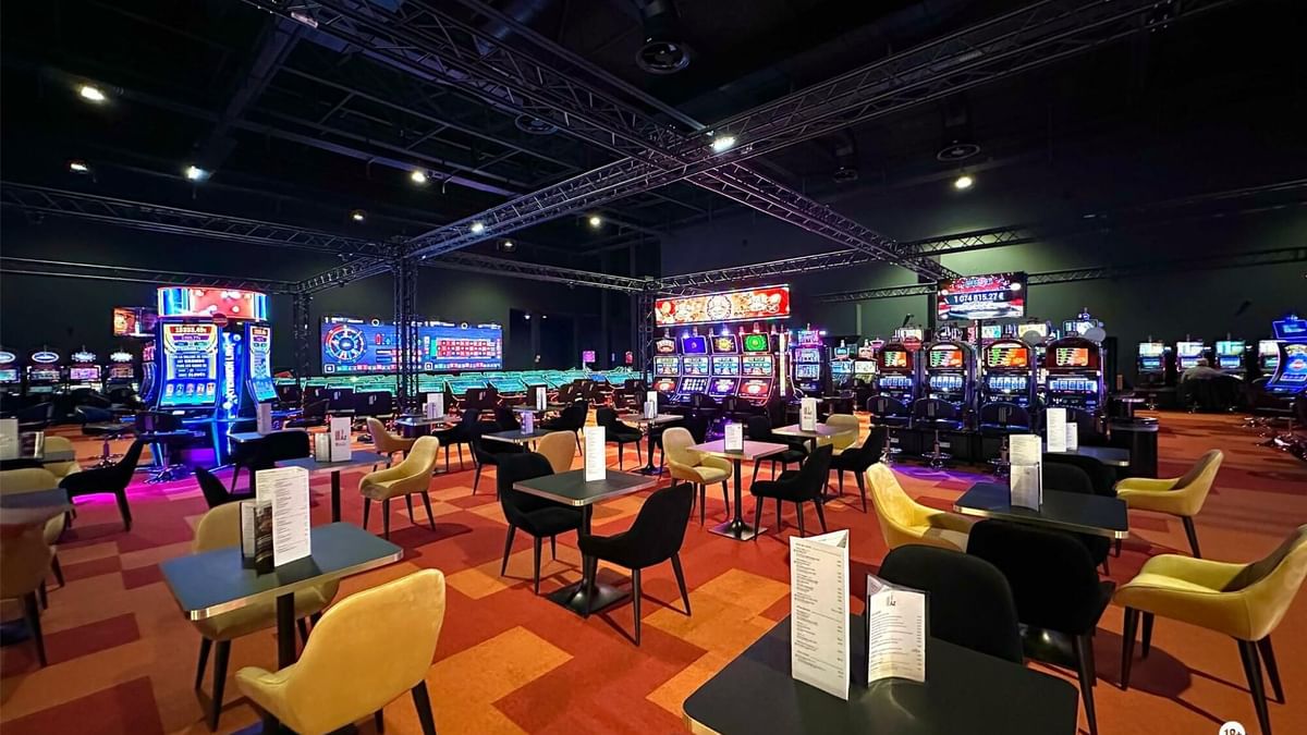 Salon de jeux avec tables et chaises, machines à sous lumineuses, et tapis au sol.