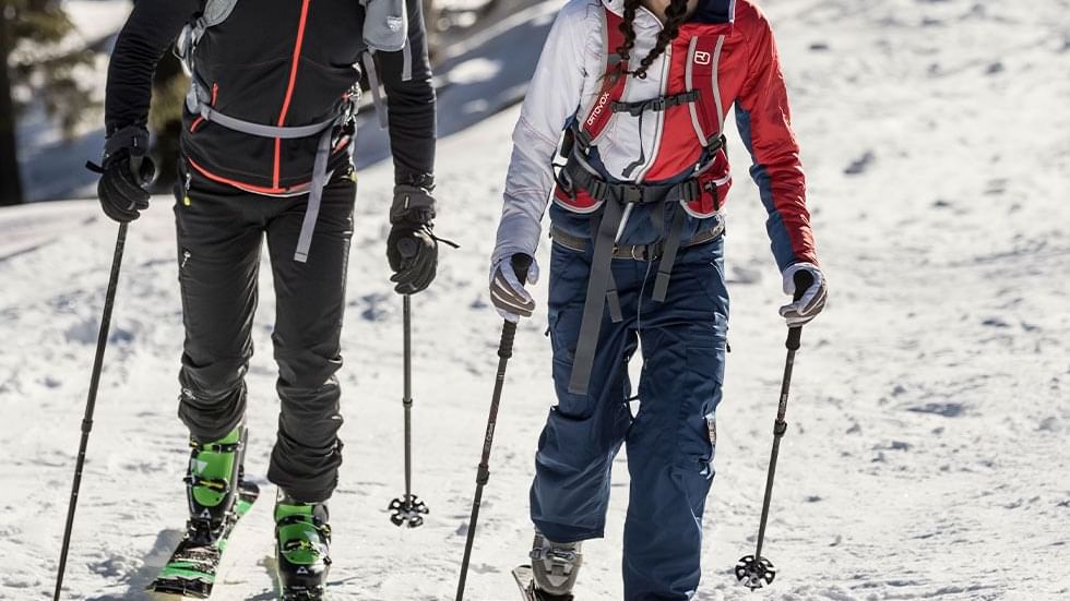 Couple in ski gear with poles walking on snow near Falkensteiner Hotel Schladming