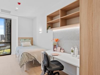 Modern room with a bed, desk, chair, and balcony at UniLodge Brisbane City.