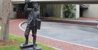 Bronze statue of a newspaper boy holding a paper outside the covered Shula\'s Hotel front entrance at Miami Lakes Hotel
