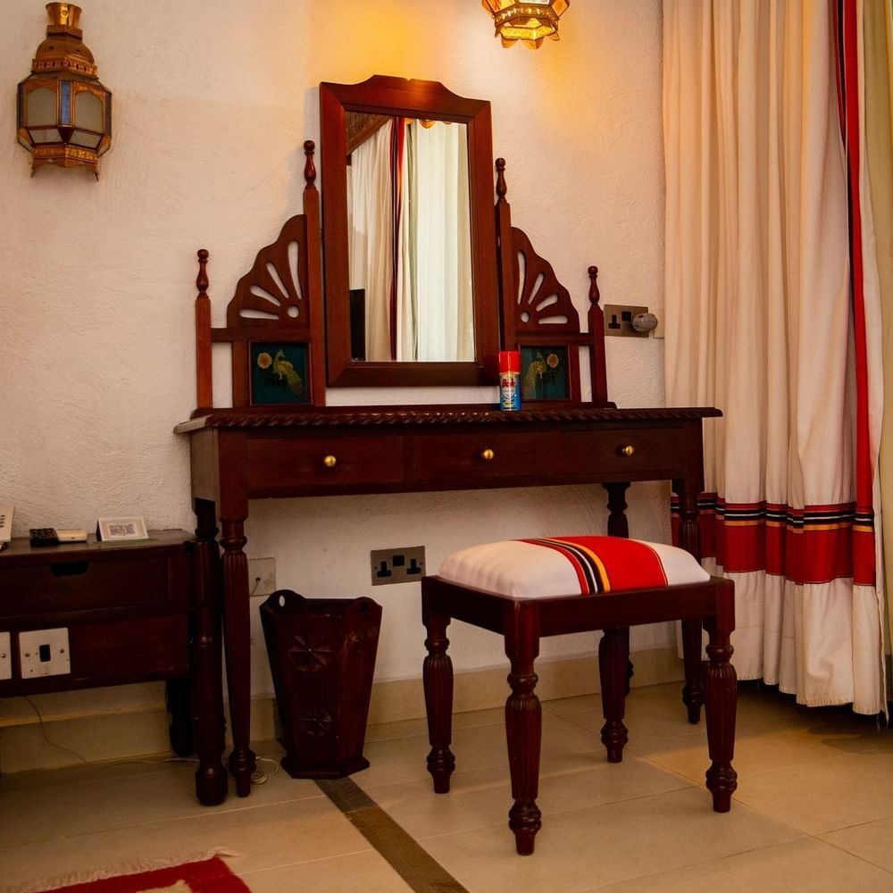 Elegantly decorated vanity area with a wooden stool and a mirror in Zanzibar Suite at Serena Beach Resort & Spa Mombasa.