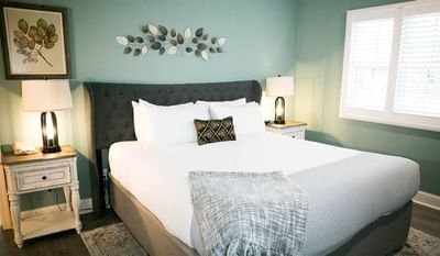 A bedroom with a bed, pillows, two nightstands with lamps, and a window with blinds.