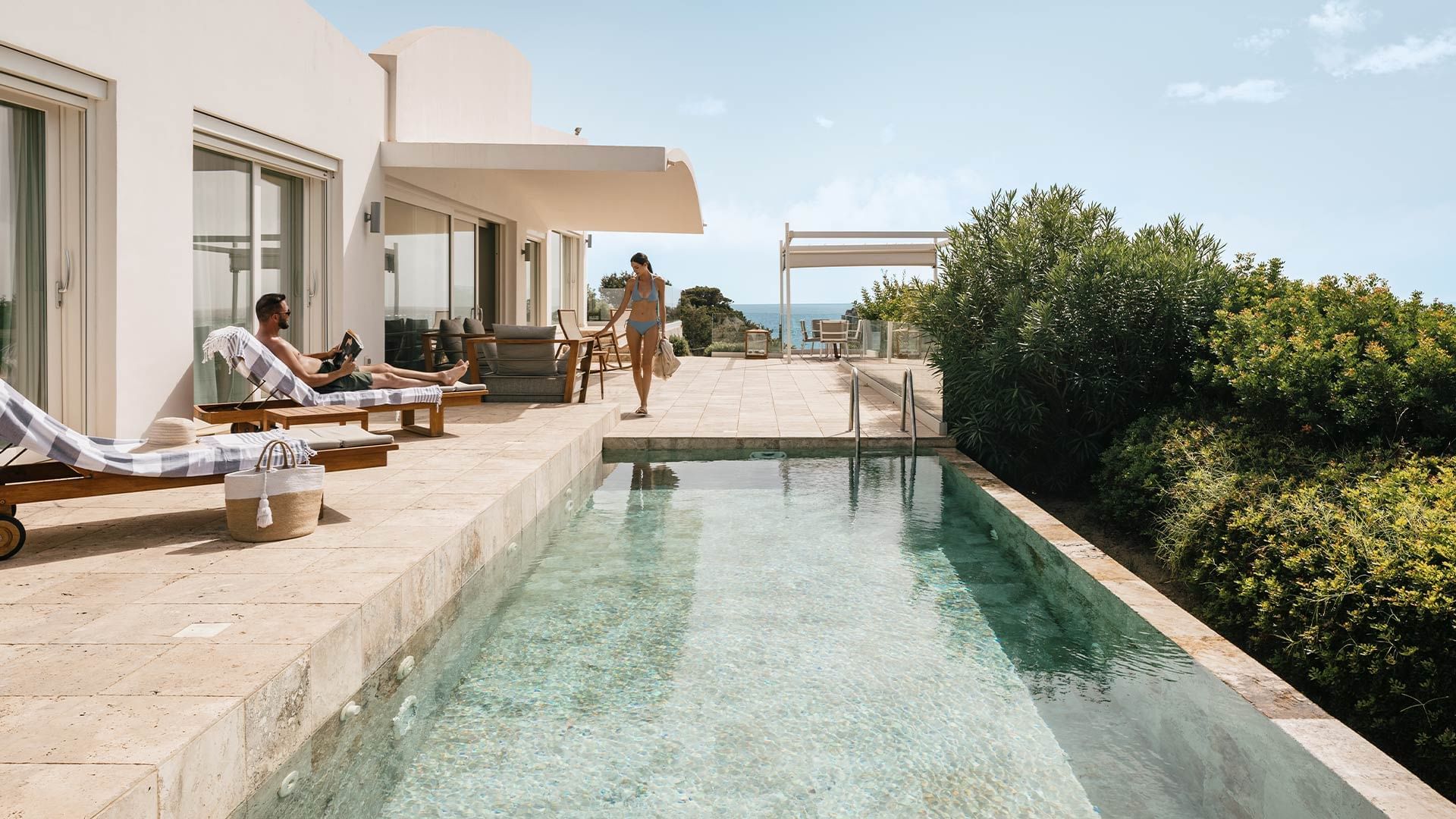 Zwei Personen genießen den Pool und die Aussicht auf das Meer von einer Terrasse umgeben von Bäumen.