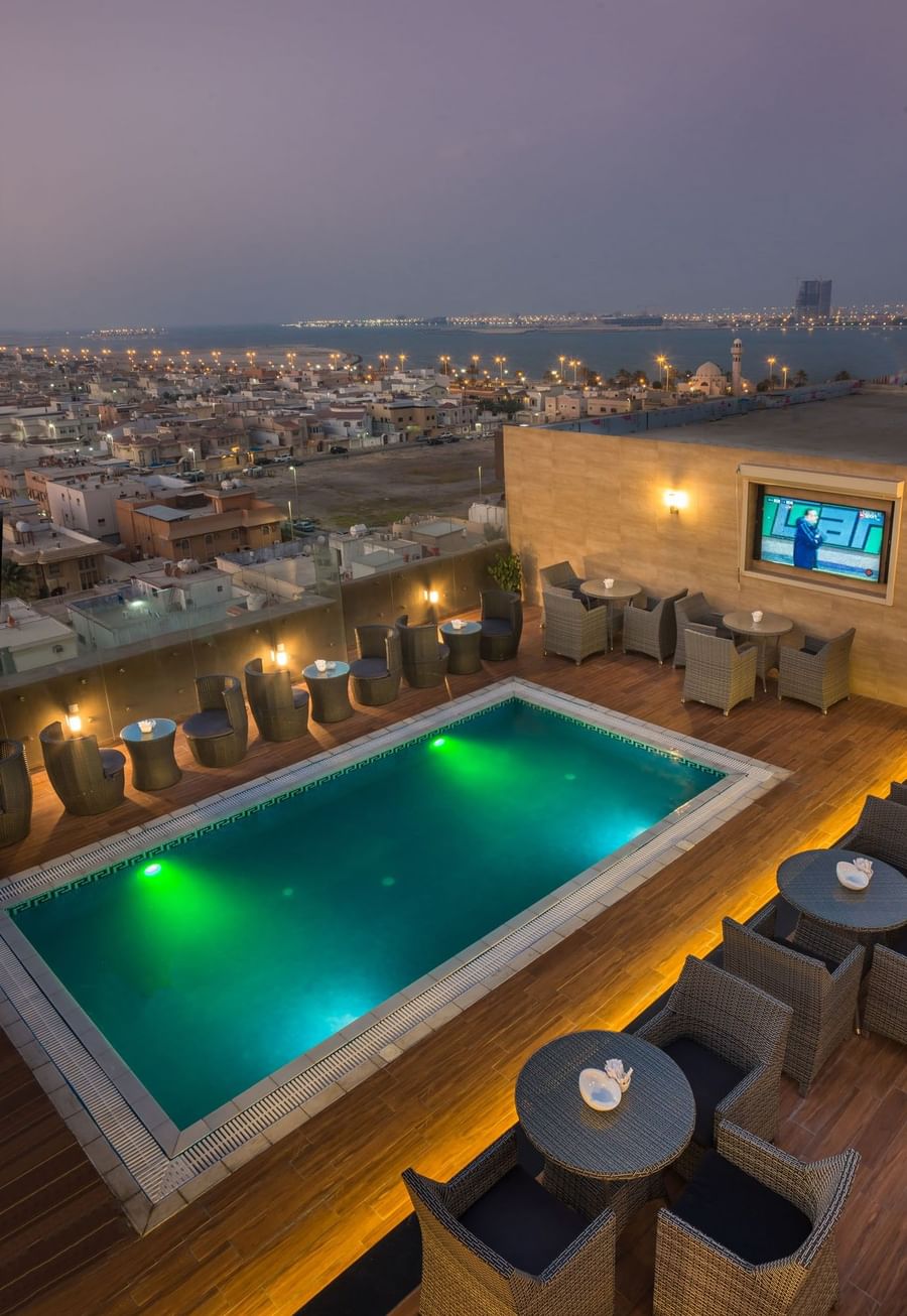 City view by rooftop pool, featuring wicker chairs surrounding tables in Sky View Café Naviti By Warwick Dammam
