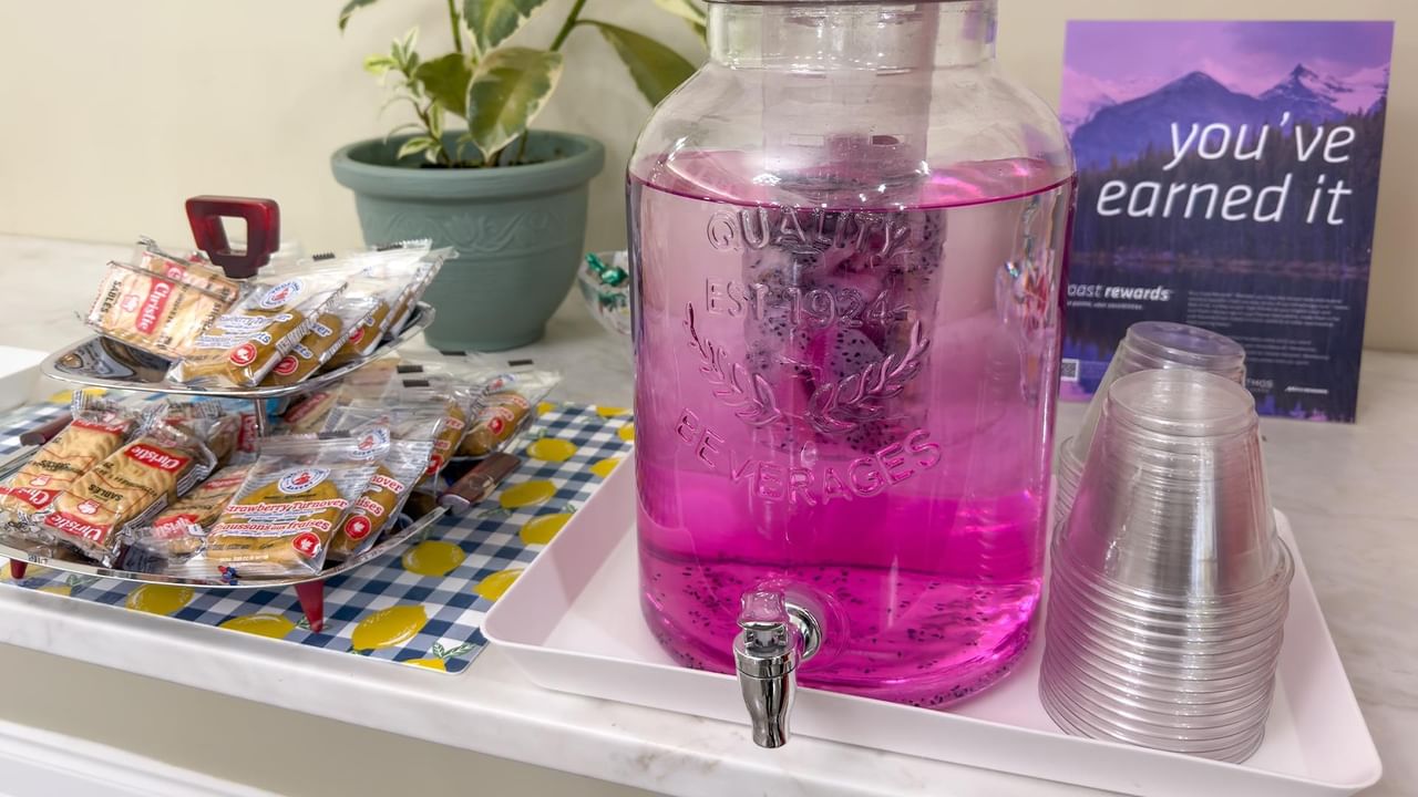 Glass beverage dispenser with pink drink, snack trays, and stacked cups at Coast Edson Hotel