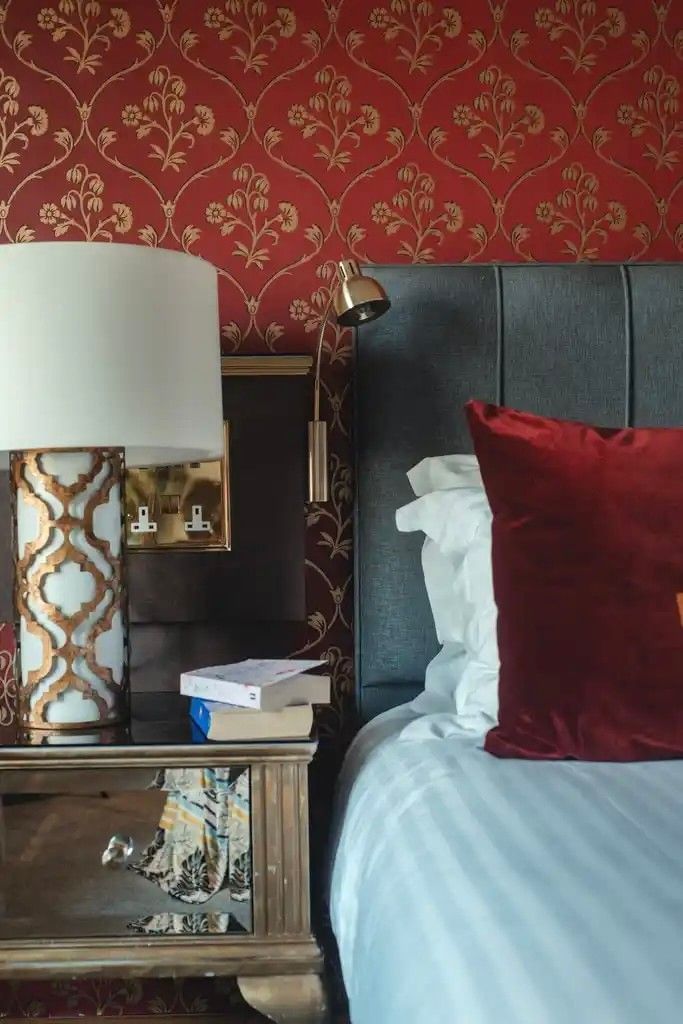Bed with red pillows by an ornate gold lamp and patterned red wallpaper for hotel rooms warwickshire at Polo Club Hotel
