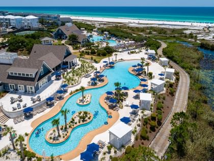 Aerial view of the Watersound Beach Club pool complex with blue loungers, white cabanas, and turquoise Gulf waters.