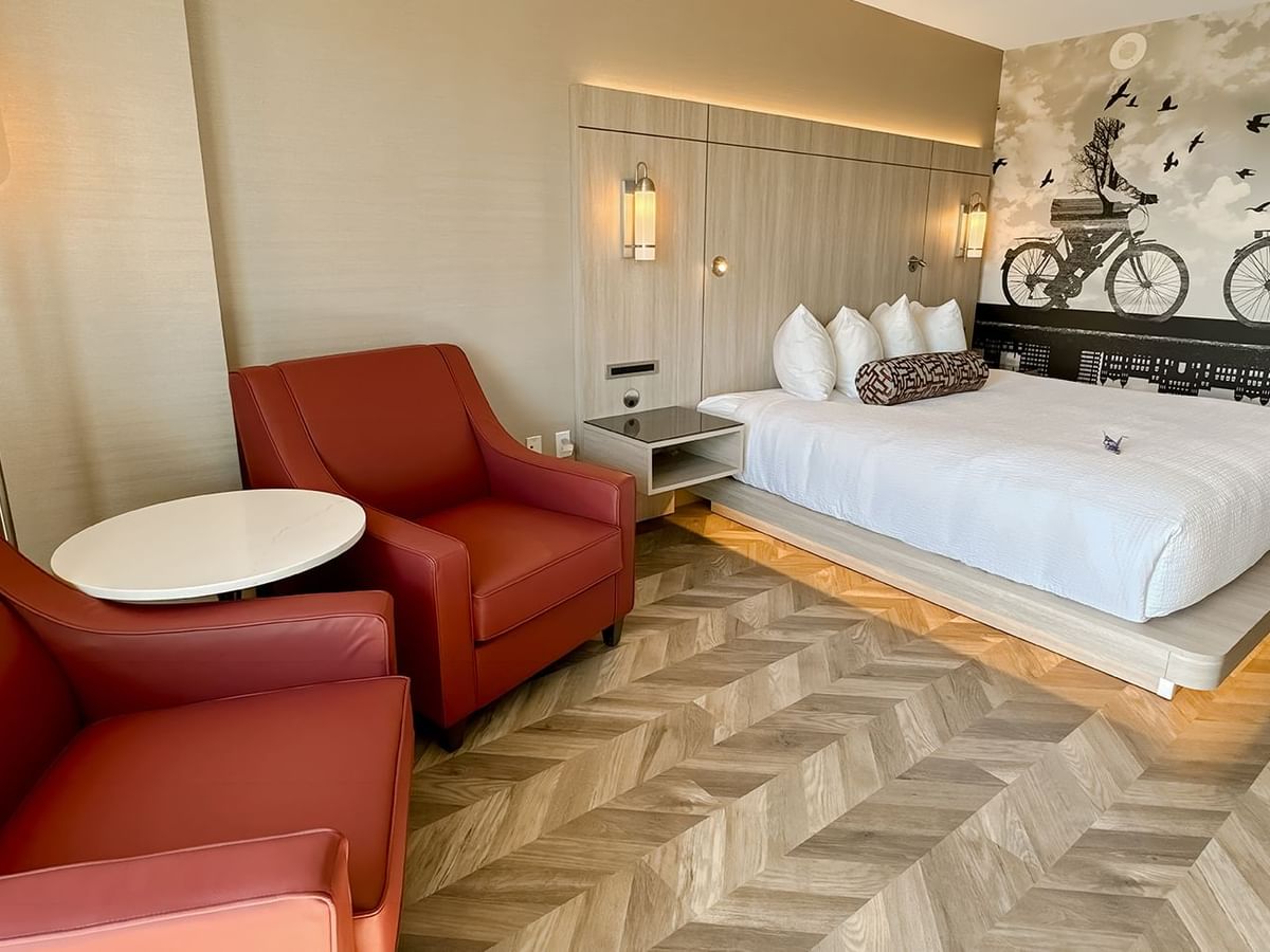 Hotel guestroom with king bed, two sofas, lamp, and nightstand.