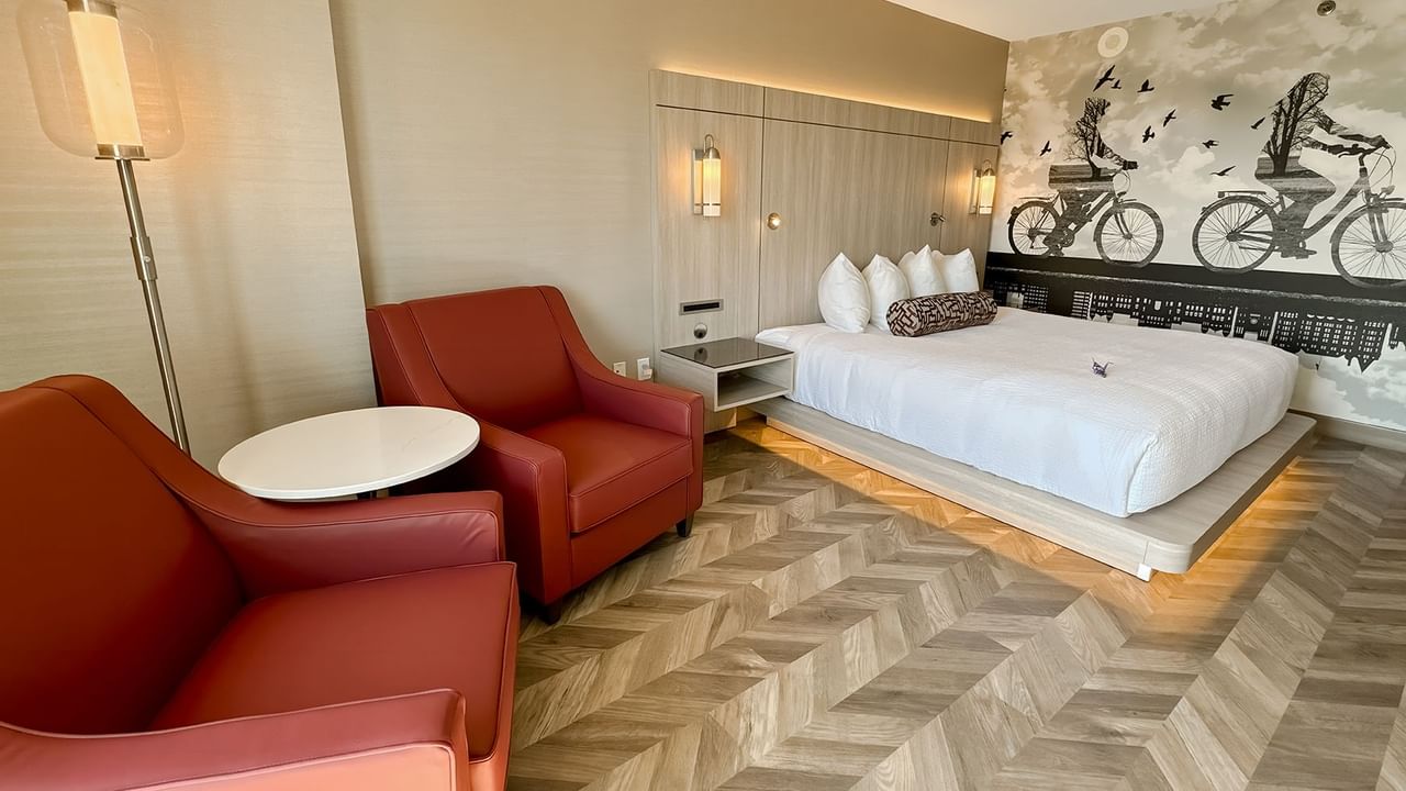 Hotel guestroom with king bed, two sofas, lamp, and nightstand.