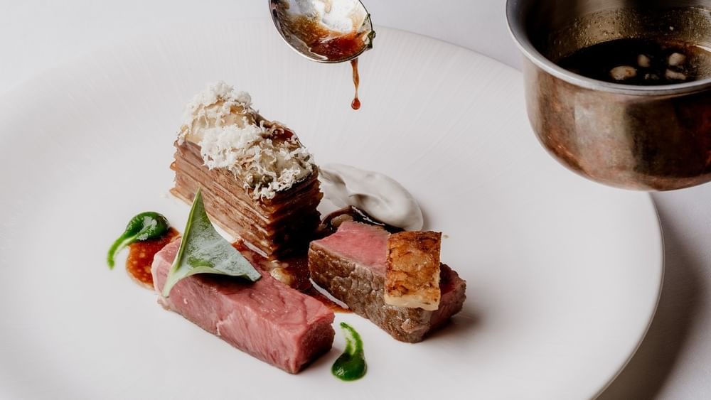 Chef using a spoon to pour sauce to a seared meat served at The Capital Hotel, Apartments and Townhouse