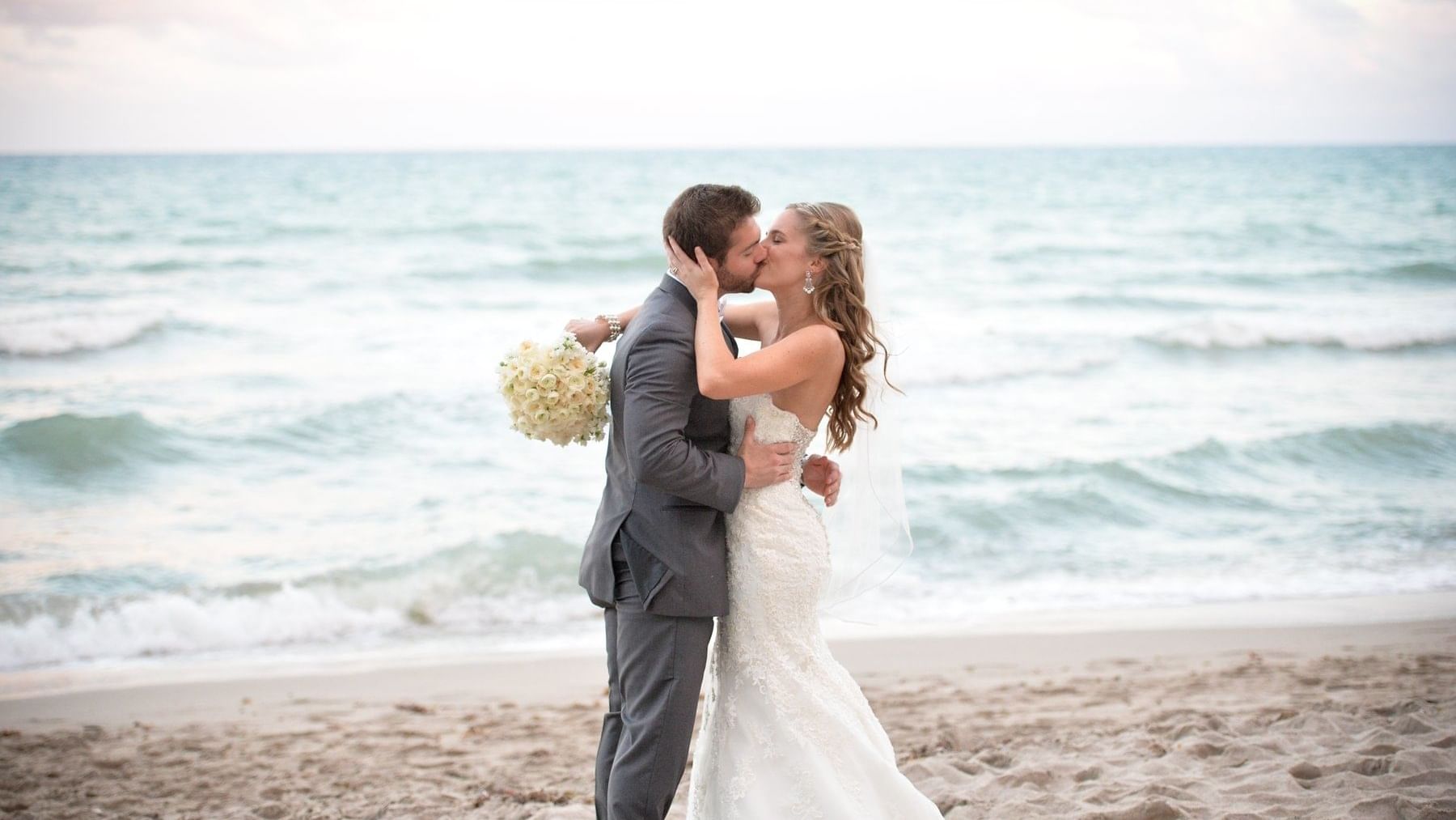 Bride and groom kissing on beach at Diplomat Beach Resort