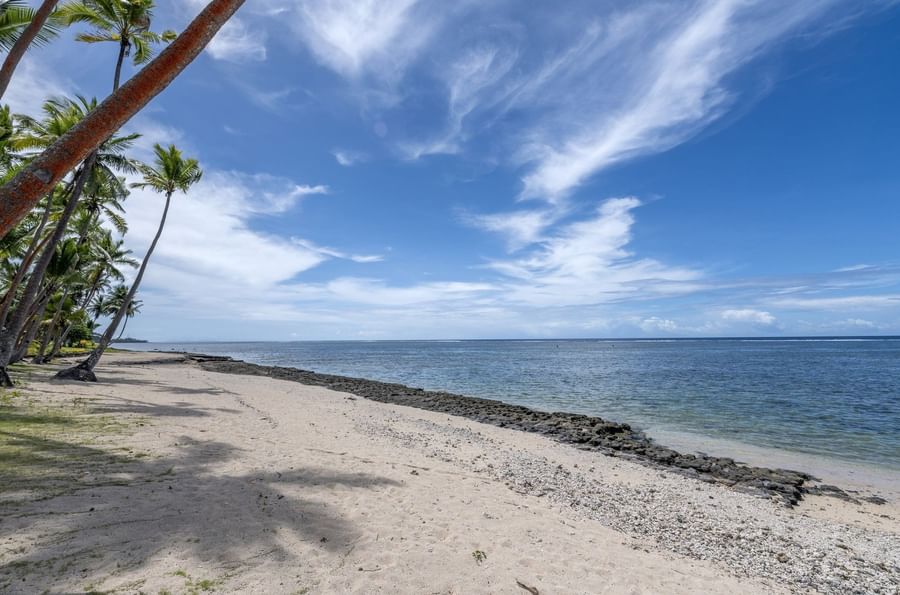 Sandy beach with a dark rock barrier by the blue ocean under a wispy cloud sky near Tambua Sands Beach Resort
