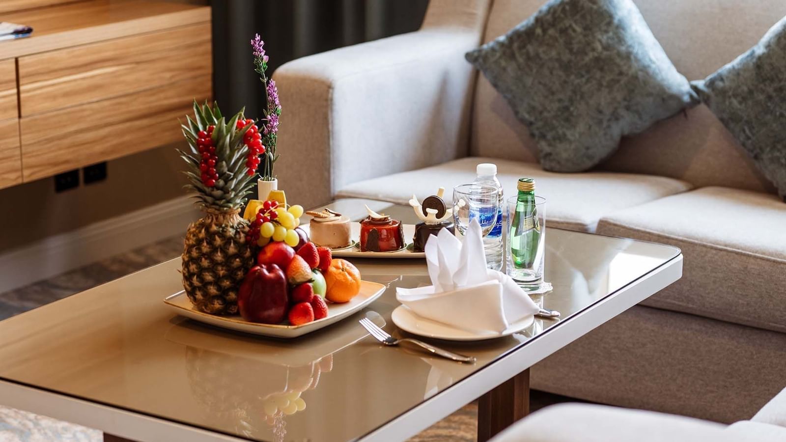 Fruit platter and pastries on a glass table by a grey sofaAl Maha Café at Cantonal Hotel by Warwick Riyadh