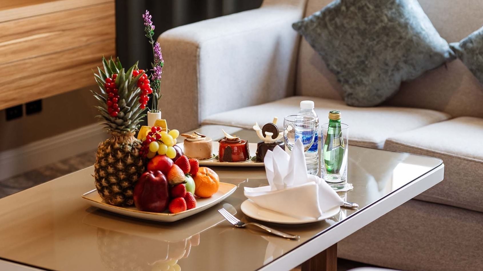 Fruit platter and pastries on a glass table by a grey sofa in The Tower View at Cantonal Hotel by Warwick Riyadh