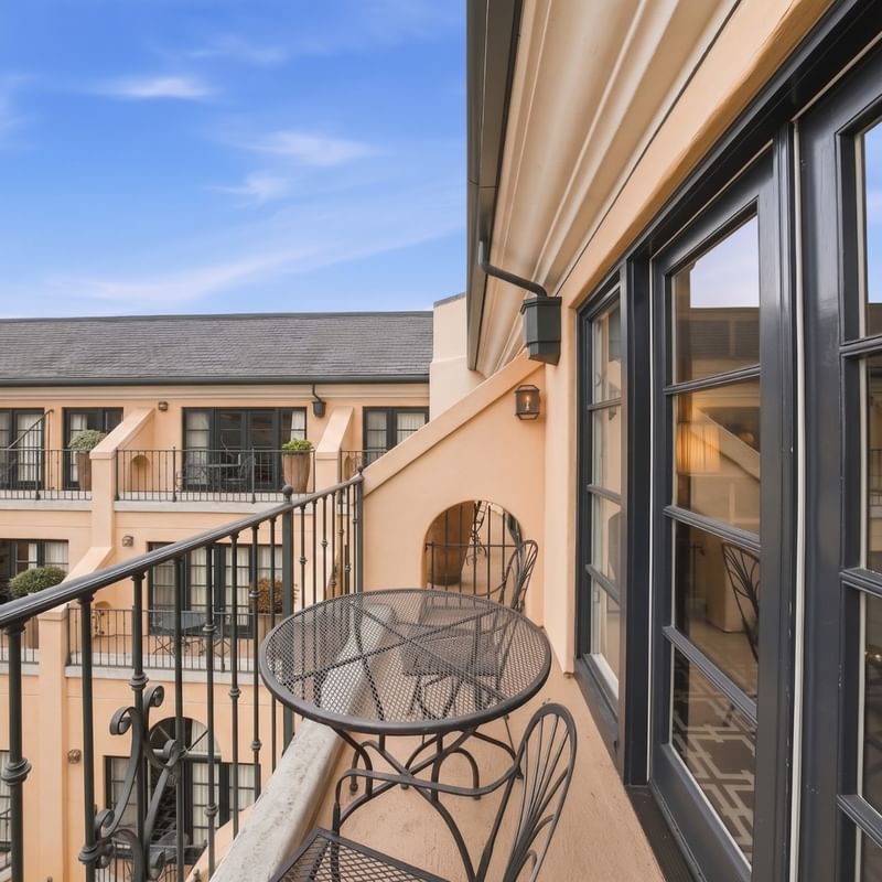 Private balcony with metal bistro table and chairs overlooking courtyard with peach-colored building facade at el PRADO Hotel