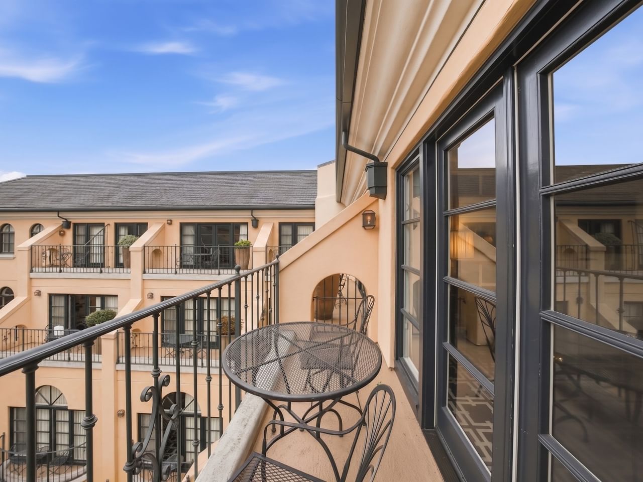 Private balcony with metal bistro table and chairs overlooking courtyard with peach-colored building facade at el PRADO Hotel
