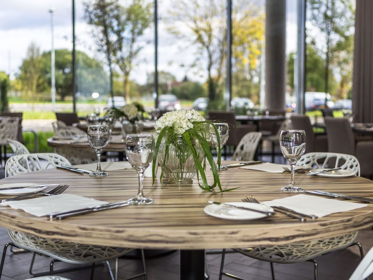 Dining table with glassware and floral centerpiece by large windows in Glass House Restaurant at Heston Hyde Hotel